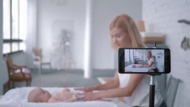 Blogger moeder leert hoe om luier pasgeboren meisje te veranderen tijdens het opnemen van training video op mobiele telefoon voor volgers in sociale netwerken — Stockvideo