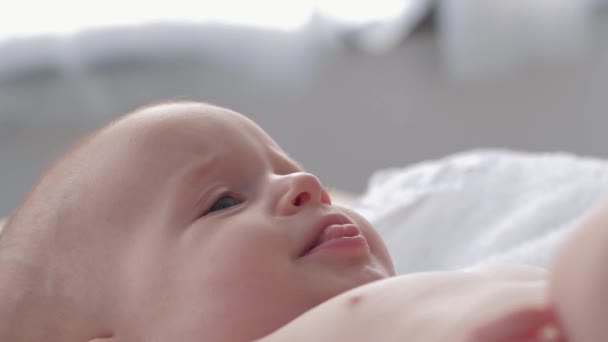 Feliz niña con hermosos ojos se encuentra en el cambio de mesa y está babeando de cerca — Vídeos de Stock