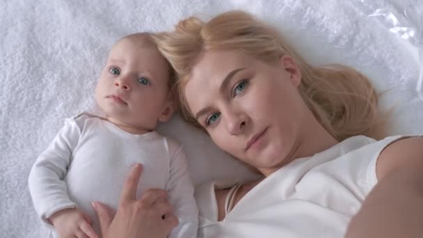 Relacionamento criança e mãe, jovem pai com uma menina doce bebê deitado na cama branca e posar na câmera de perto — Vídeo de Stock