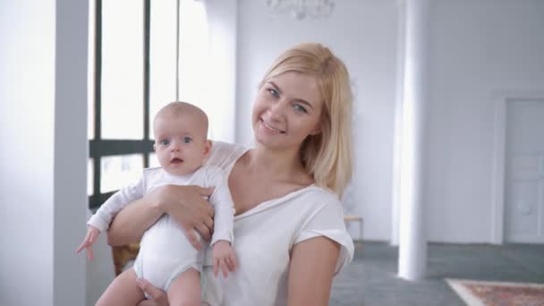 Retrato de la familia, mamá linda sacude a su hija recién nacida en sus brazos y sonríe a la cámara — Vídeos de Stock