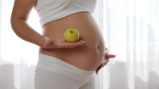 Питание и диета во время беременности, женщина с ребенком в животе держит в руке зеленое яблоко — стоковое видео