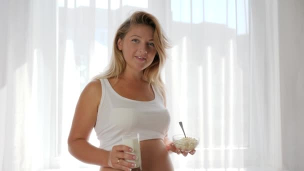 Портрет красивой беременной женщины, держащей молоко в стакане и тарелку с творогом — стоковое видео