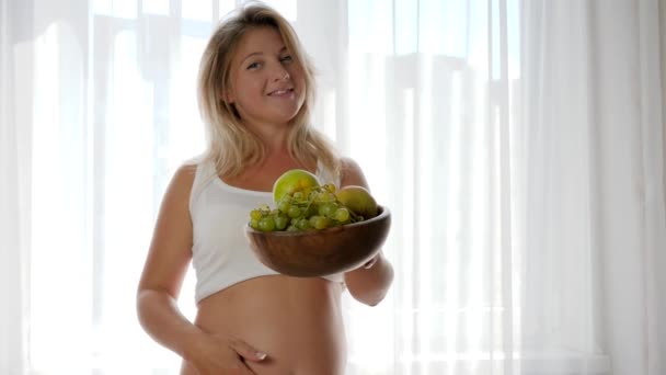 Portrait of woman with naked abdomen smil and holds dish with fresh fruits — Stock Video