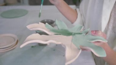 Sanat atölyesinde yeni bitirilmiş çömlekçi tabağının üzerinde fırçayla çizim yapan zanaatkar elleri