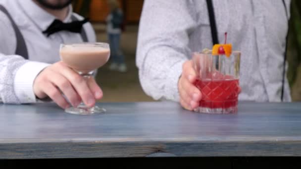 Two barmen serves alcohol, barkeeper decorated colored drinks on bar counter, in hands bartenders chilled drinks — Stock Video