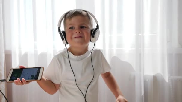 Mignon garçon dans les écouteurs avec téléphone dans les mains écouter de la musique et danser — Video