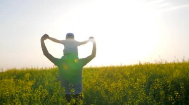 Aile yürüyüşü, boynunda çocuk olan erkekler tarlada yürüyor, baba ve çocuklar kollarını kaldırarak tarlaya gidiyorlar.,