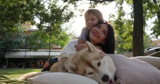 Rodzina i zwierzak, młoda matka z dzieckiem leżą w pobliżu husky pies na tle natury zbliżenie — Wideo stockowe