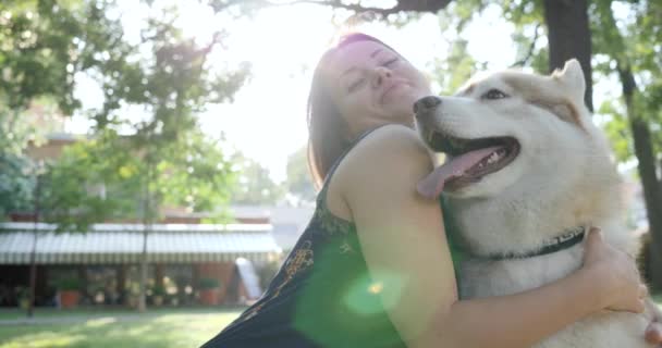 Genç kadın gülümsüyor ve parkta köpeğe sarılıyor. Mutlu evcil hayvan ev sahibesinin yanında eğleniyor. — Stok video