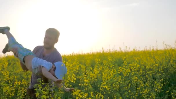 Alegre niño a manos de padres en forma de avión en el campo, papá con hijo en brazos jugado en flores de prado , — Vídeo de stock