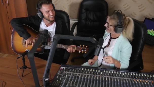 Cheerful guy in headset playing on musical instrument next to radio presenter near audio console in room — Stock Video