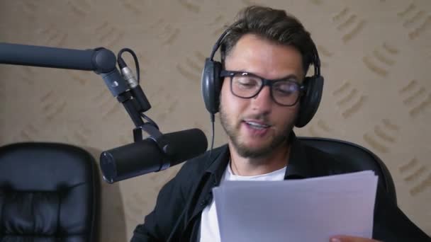 Presentador de radio en gafas y auriculares habla en el micrófono — Vídeos de Stock