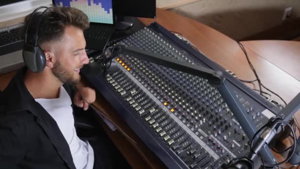 DJ com fones de ouvido na cabeça sentar na cadeira e trabalha perto mixer — Vídeo de Stock