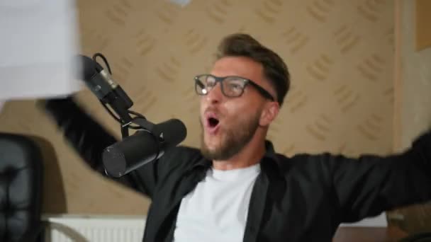 Эмоциональный парень в очках машет руками и разбрасывает бумагу в помещении — стоковое видео