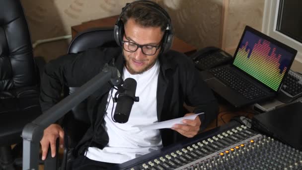 Mann mit Kopfhörer und Blatt Papier spricht in Mikrofonnähe im Radiostudio — Stockvideo