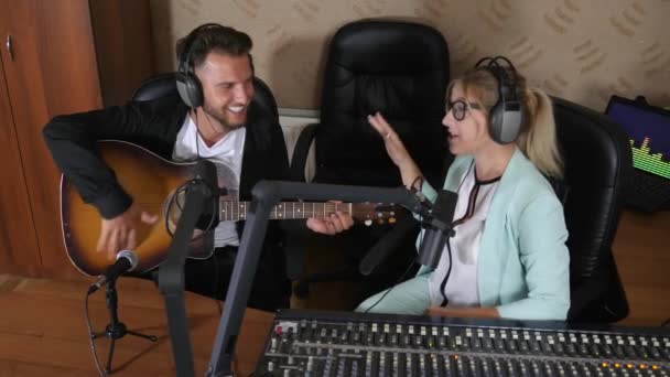 Ευτυχισμένη γυναίκα με ακουστικά σε συνέντευξη με τον τύπο που παίζει κιθάρα στο στούντιο — Αρχείο Βίντεο