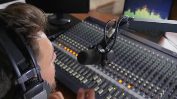 Trabajo en la radio, hombre en auriculares habla en micrófono al lado de la consola de audio — Vídeos de Stock