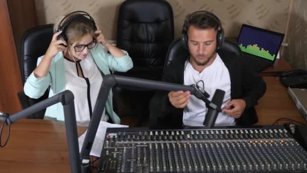 Άνδρας και γυναίκα με ακουστικά επικοινωνούν μεταξύ τους κατά τη διάρκεια της εργασίας δίπλα στο μικρόφωνο και την κονσόλα — Αρχείο Βίντεο