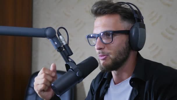 Hombre anfitrión de radio en gafas y auriculares dice en Mike en el estudio — Vídeos de Stock