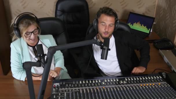 Vrolijk radio host man en vrouw spreken in microfoon in de buurt audio mixer in de studio — Stockvideo