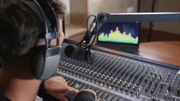 Гарний радіо-хост у навушниках розмовляє мікрофоном і робить звук голоснішим на мікшерній консолі в студії — стокове відео