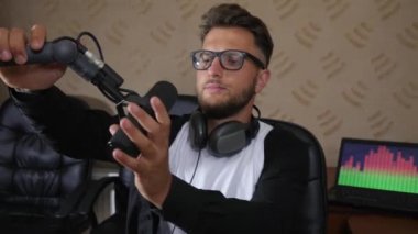 Gözlüklü ve kulaklıklı pozitif adamlar canlı yayında ses konsolunun yanındaki mikrofona yönlendiriyor.