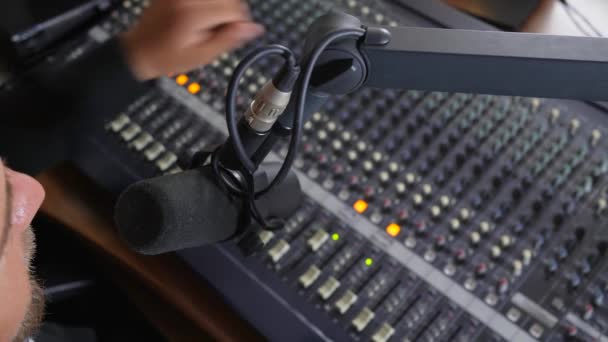 Hombre positivo en auriculares habla en el micrófono y hace que el sonido más fuerte en el equipo en el estudio de radio — Vídeo de stock