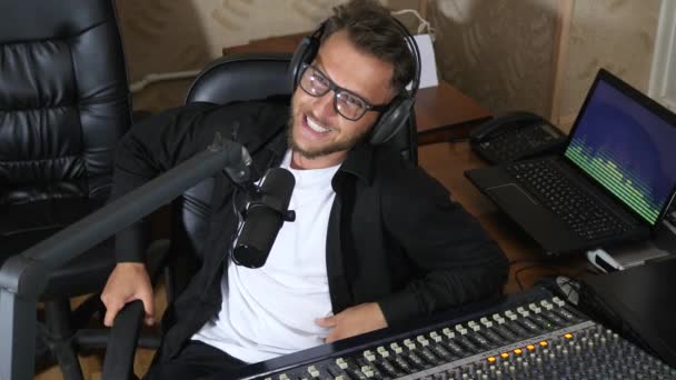 Rádió műsorvezető szemüvegben beszél mikrofonba mellett keverő konzol — Stock videók