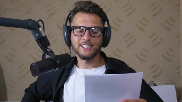 Felvétel stúdió, közelről fiatal férfi szemüvegben felolvassa a szöveget mikrofonba, miközben dolgozik a rádión — Stock videók