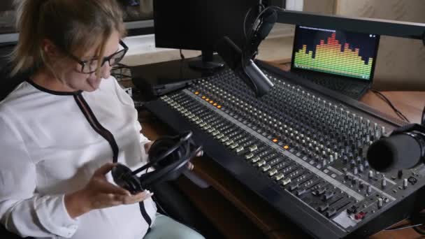 Mujer sostiene los auriculares en la barriga grande en el estudio de radio, trabajo dañino — Vídeos de Stock