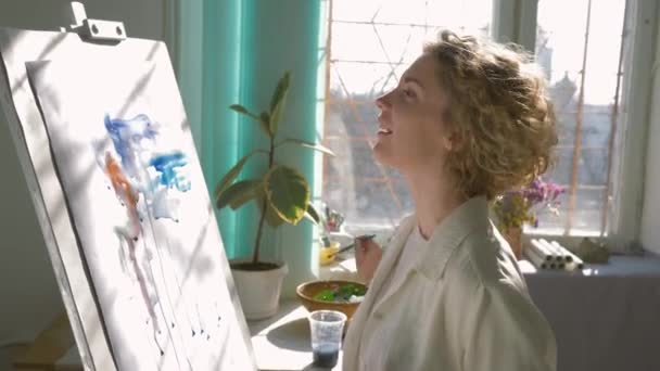 Inspiração artista criativo, mulher artesão feliz com pintura musa imagem com cores brilhantes na tela branca no cavalete dentro de casa — Vídeo de Stock