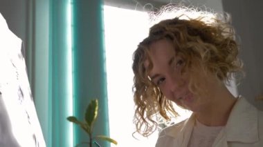 İlham perili ressam kız, resim sehpasında fırçayla resim çizer. Sanat dersinde doğal ışıkta pencereye karşı.