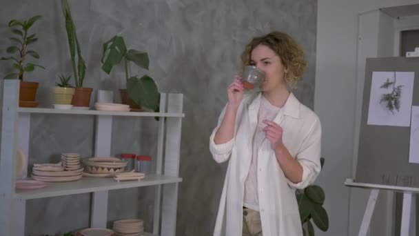 Inspiráló atmoszféra, fiatal fazekas női inni forró tea csésze, miközben dolgozik agyag kézműves műhely — Stock videók
