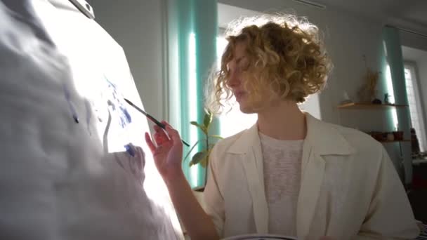 Ταλαντούχος ζωγράφος γυναίκα με έμπνευση αντλεί με πινέλο εικόνα σε καμβά στο στούντιο τέχνης στο φυσικό φως ενάντια στο παράθυρο — Αρχείο Βίντεο