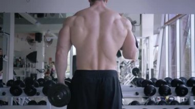 Profesyonel sporlar, güçlü kaslı bir adam spor merkezinde ayna önünde güç antrenmanı yaparken kollarında dambıllarla egzersiz yapıyor.