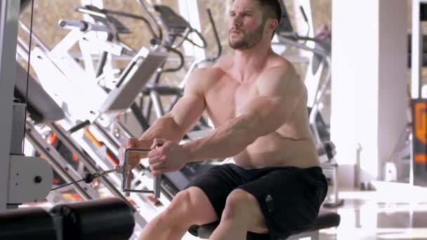Sporttraining, starker Bodybuilder-Typ sitzt beim Muskelaufbautraining auf einem Traktionssimulator für Hände, während er im Fitnessstudio an seinem Körper arbeitet — Stockvideo