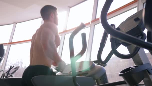 Hälsosam livsstil, naken sportkille med stora muskler som springer på löpband under konditionsträning på gym mot fönster i starkt naturligt ljus — Stockvideo