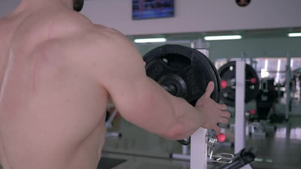 Sportclub, spieropbouwer met blote borst zet schijf op lange halter om te bankdrukken tijdens sportkrachttraining in fitnessclub — Stockvideo