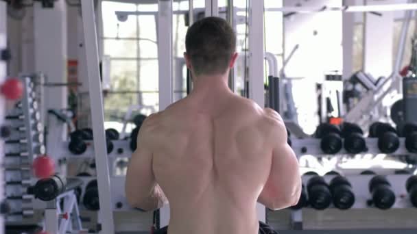 Sterke bodybuilder man voert een oefening voor spieropbouw training op tractie simulator voor armen tijdens het werken op het lichaam in de sportschool — Stockvideo