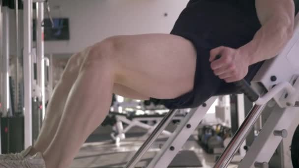 Güçlü kaslı sporcu spor merkezinde kas geliştirme eğitimi sırasında bacak baskı makinesi üzerinde egzersiz yapar. — Stok video