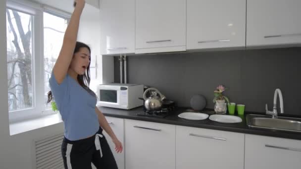 Счастливая смешная домохозяйка балуется и поет с тарелками на руках на кухне дома — стоковое видео