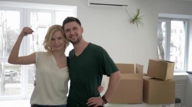 Yeni eve taşınma, gülümseyen sevgililerin portresi. Kız gibi giyinen sevgililer. Dairenin anahtarlarını gösterip, yeni eve taşınırken arka planda sarılıyorlar.