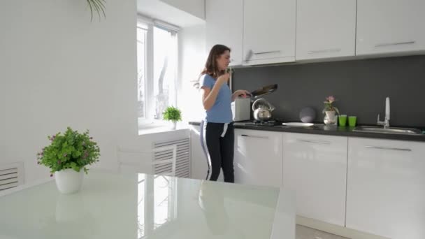 Kuchnia zabawa, wesoła gospodyni kobieta taniec i śpiewa z patelni w rękach podczas gotowania posiłek w kuchni w domu — Wideo stockowe