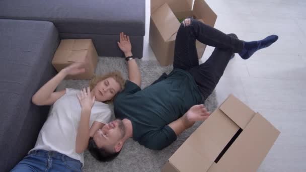 Family relocation, happy attractive guy with girl are lying on floor among boxes and dream about future home improvement to new flat — Stock Video