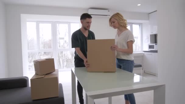 Mejoras en el hogar, el joven marido y la esposa sacando flores de la caja para decorar un nuevo apartamento durante la inauguración de la casa — Vídeo de stock