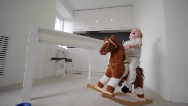 Kind ontwikkeling, schattige lieve baby jongen rijden pluche paard en glimlachen thuis in de kamer — Stockvideo