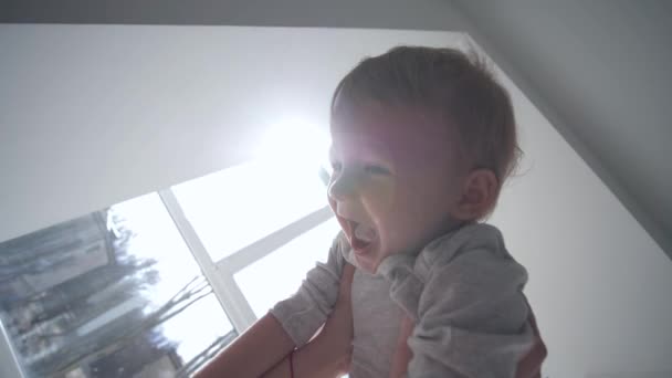Счастливое детство, улыбающийся веселый младенец в материнские руки, летящие в воздухе к окну — стоковое видео