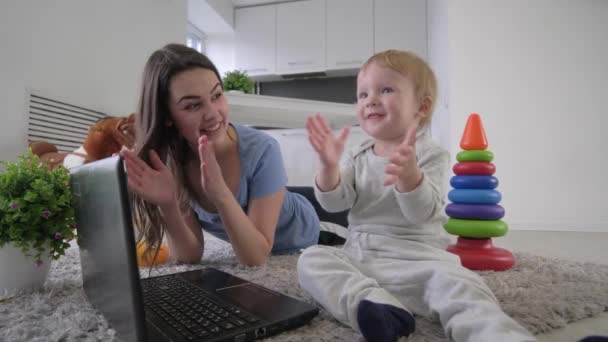 Mutlu bir aile, küçük tatlı bir çocuk ve genç bir anne dizüstü bilgisayarda yerde uzanan çizgi filmleri izlerken el çırpıyor. — Stok video