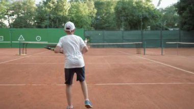 Profesyonel tenis, genç tenisçiler erkek ve kız, kırmızı sahada top ve raketlerin yardımıyla spor yapıyorlar.