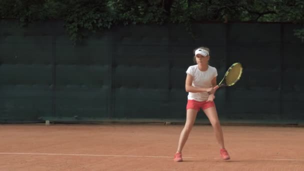 Ambitny zdeterminowany nastolatek dziewczyna tenisista z konkurencyjnego ducha koncentrując się i koncentrując się na grze i rakieta hit piłkę na czerwonym korcie — Wideo stockowe